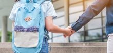 A child holds hands with a parent while walking to school.